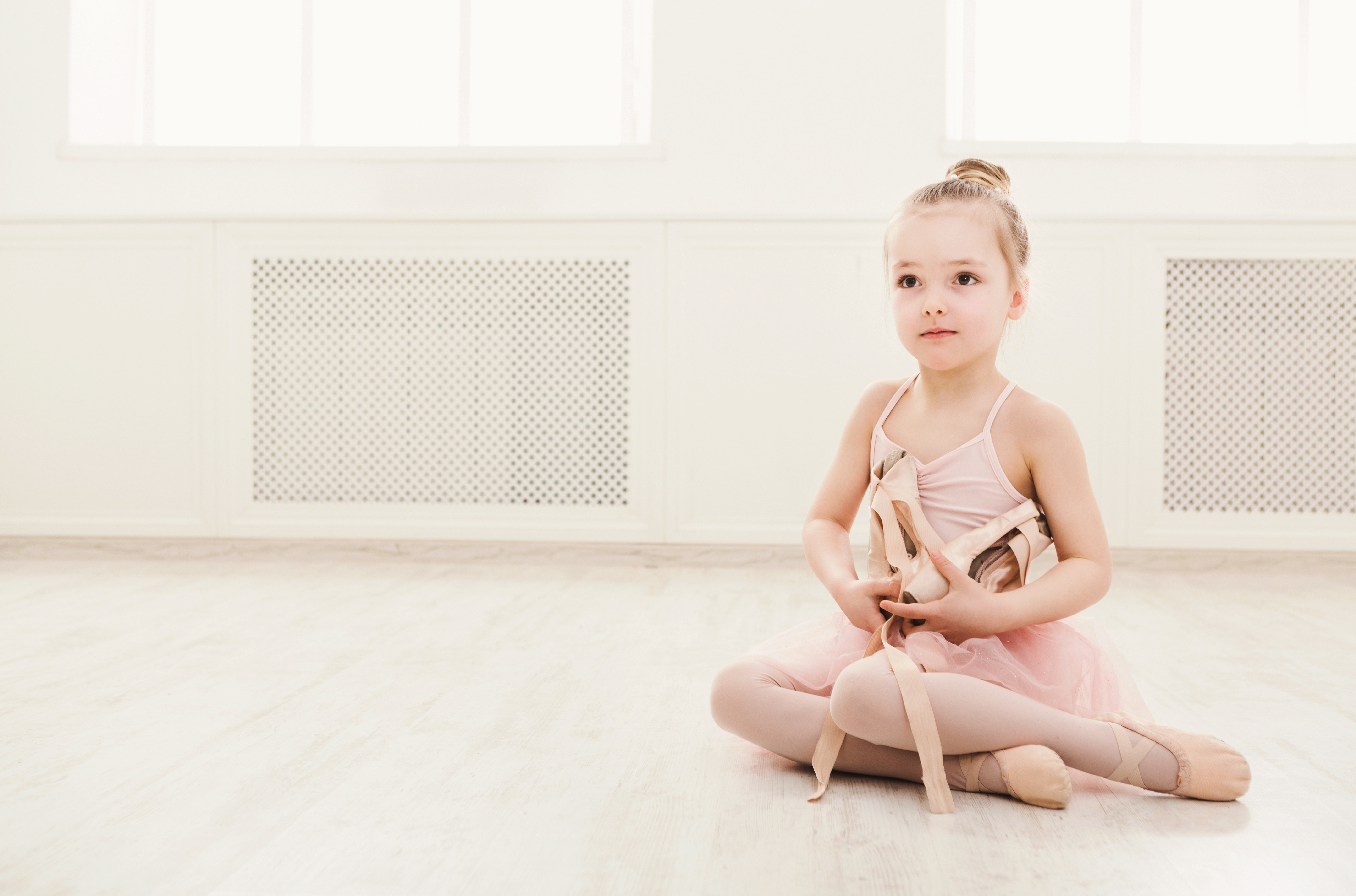 Portrait of little ballerina on floor, copy space. Smiling baby girl dreaming to become professional ballet dancer, classical dance school